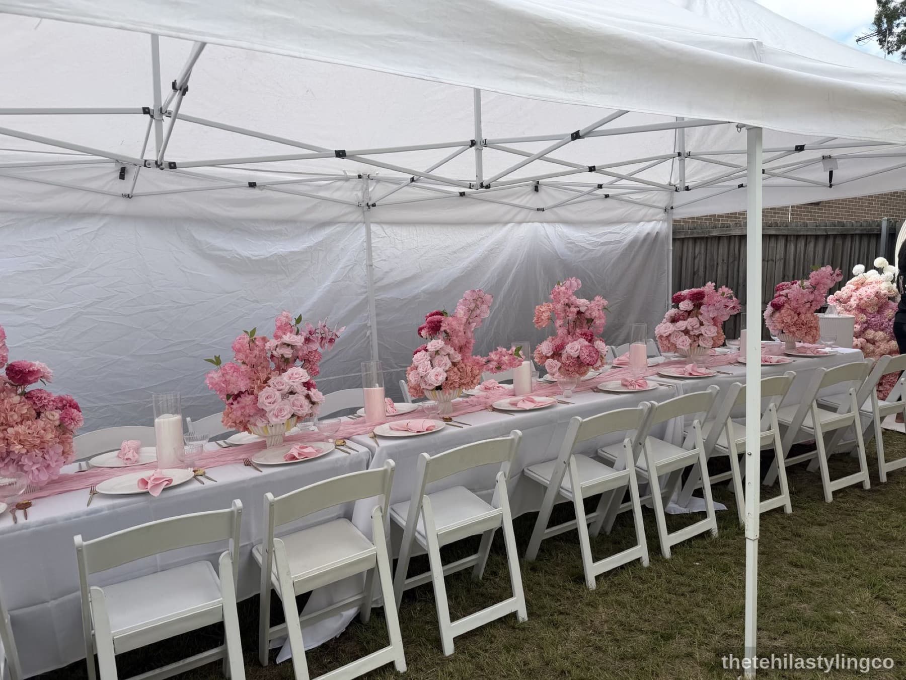 Outdoor table with pink florals, candles, and gold cutlery